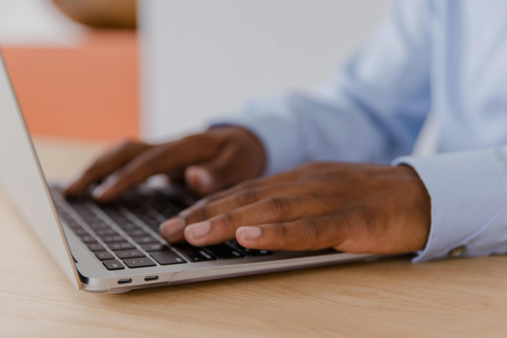 Close-up of a man's hands working on a laptop in an office setting, focused on productivity.
