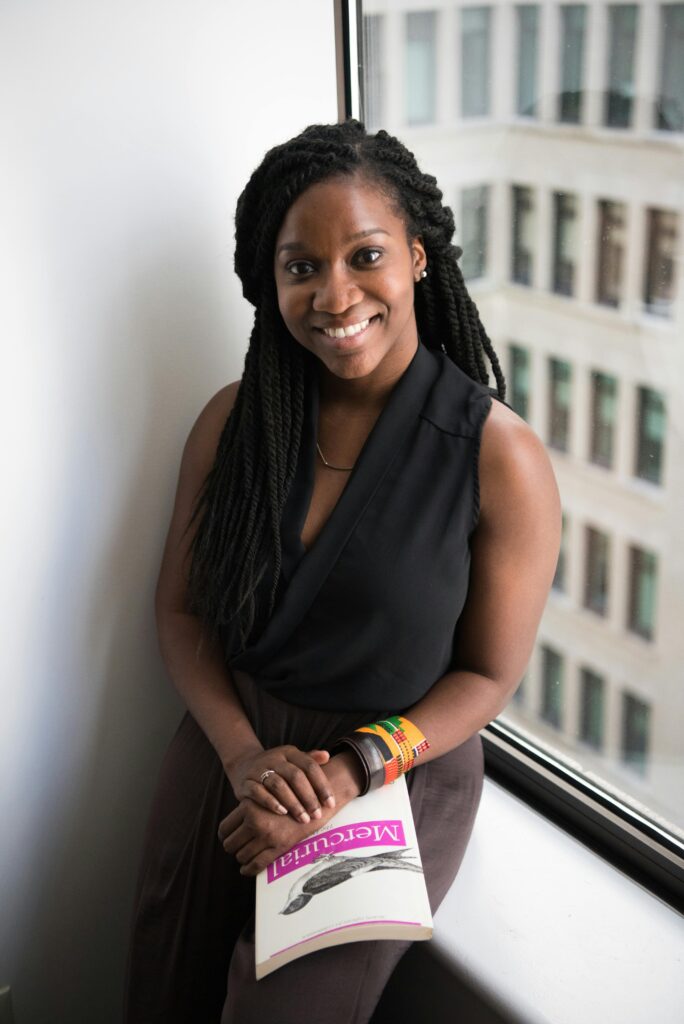 Confident young woman smiling with a book by the window in an office building.
