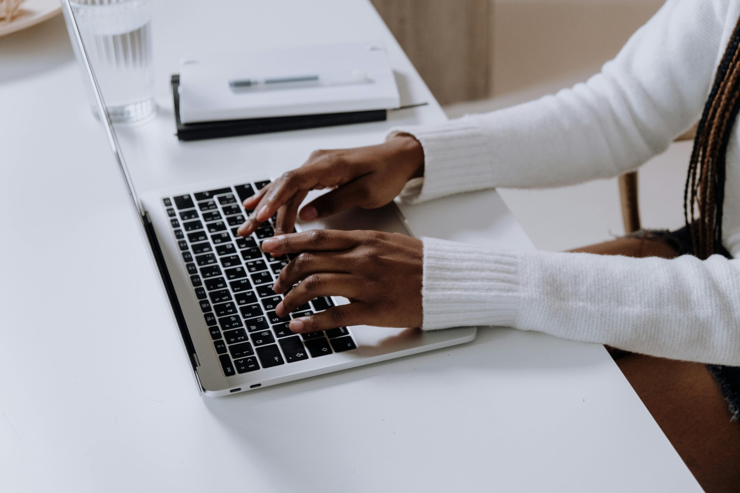 Close-up of woman's hands typing on a laptop in a modern home office setting.